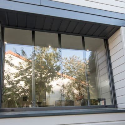 Maison avec bardage gris et fenêtre PVC gras anthracite, équipée de petits-bois verticaux intégrés.
