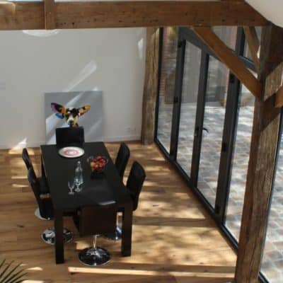 Salle à manger avec poutre apparente en bois, parquet et des fenêtres aluminium en ensemble composé.
