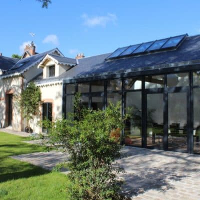 Ancienne bâtisse rénovée avec des portes fenêtres en aluminium donnant accès au jardin et une verrière pour apporter de la lumière naturelle.