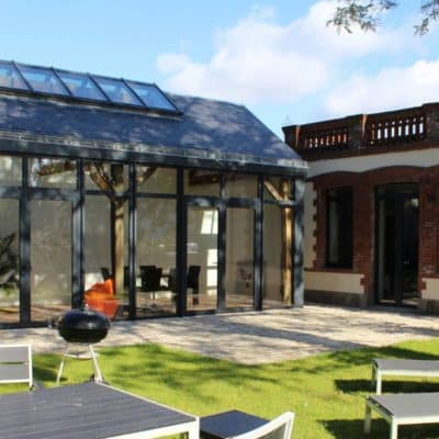 Ancien corps de ferme réhabilité en salon avec une verrière aluminium et des portes fenêtres aluminium en gris anthracite.