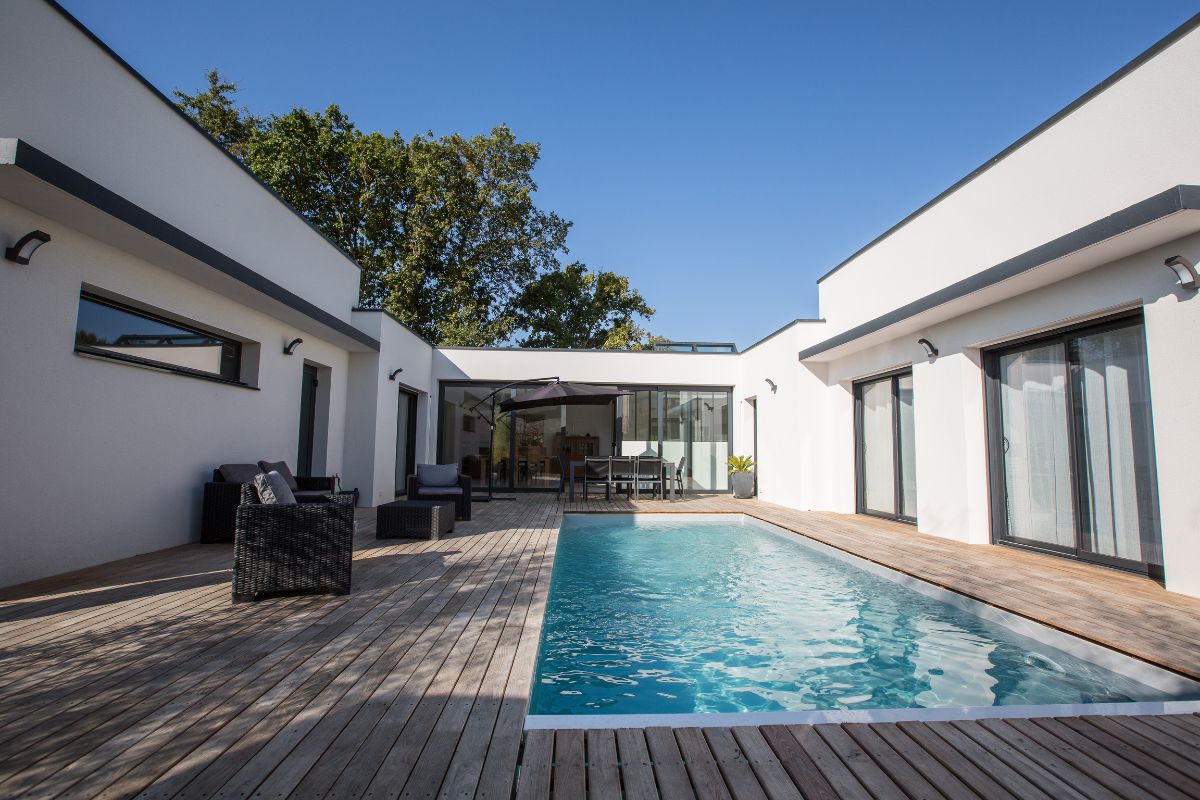 Maison neuve avec une terrasse centrale et une piscine,. La maison est équipée de baies vitrée aluminium, de fenêtres et d'une verrière de toit.