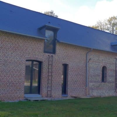 Maison en brique avec un toit en ardoise, rénovée avec des fenêtres et portes fenêtres en aluminium.
